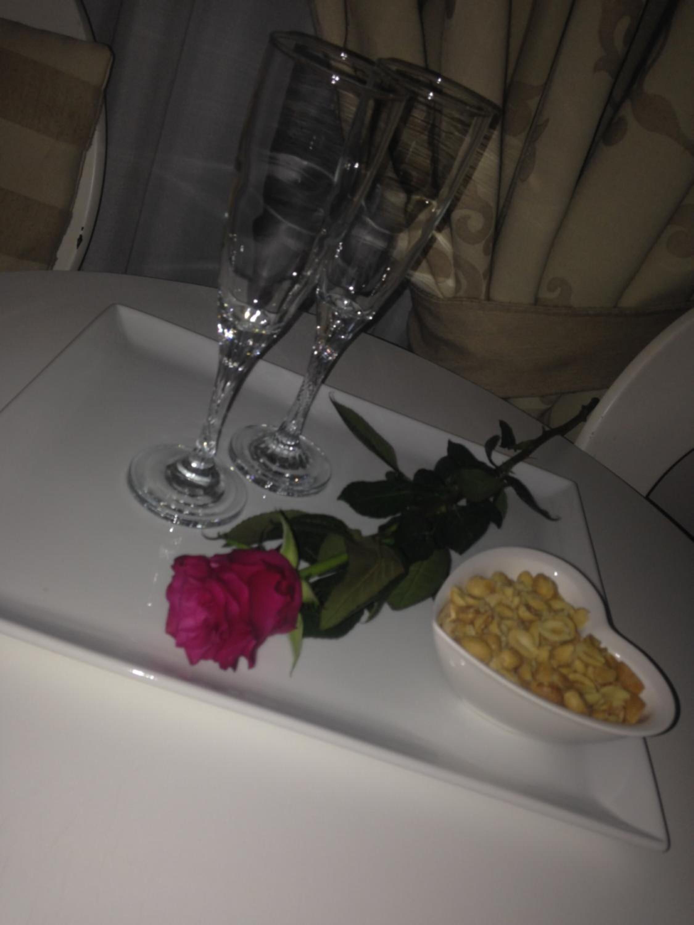 A table with two clear glasses, a single rose, and a small dish of food.