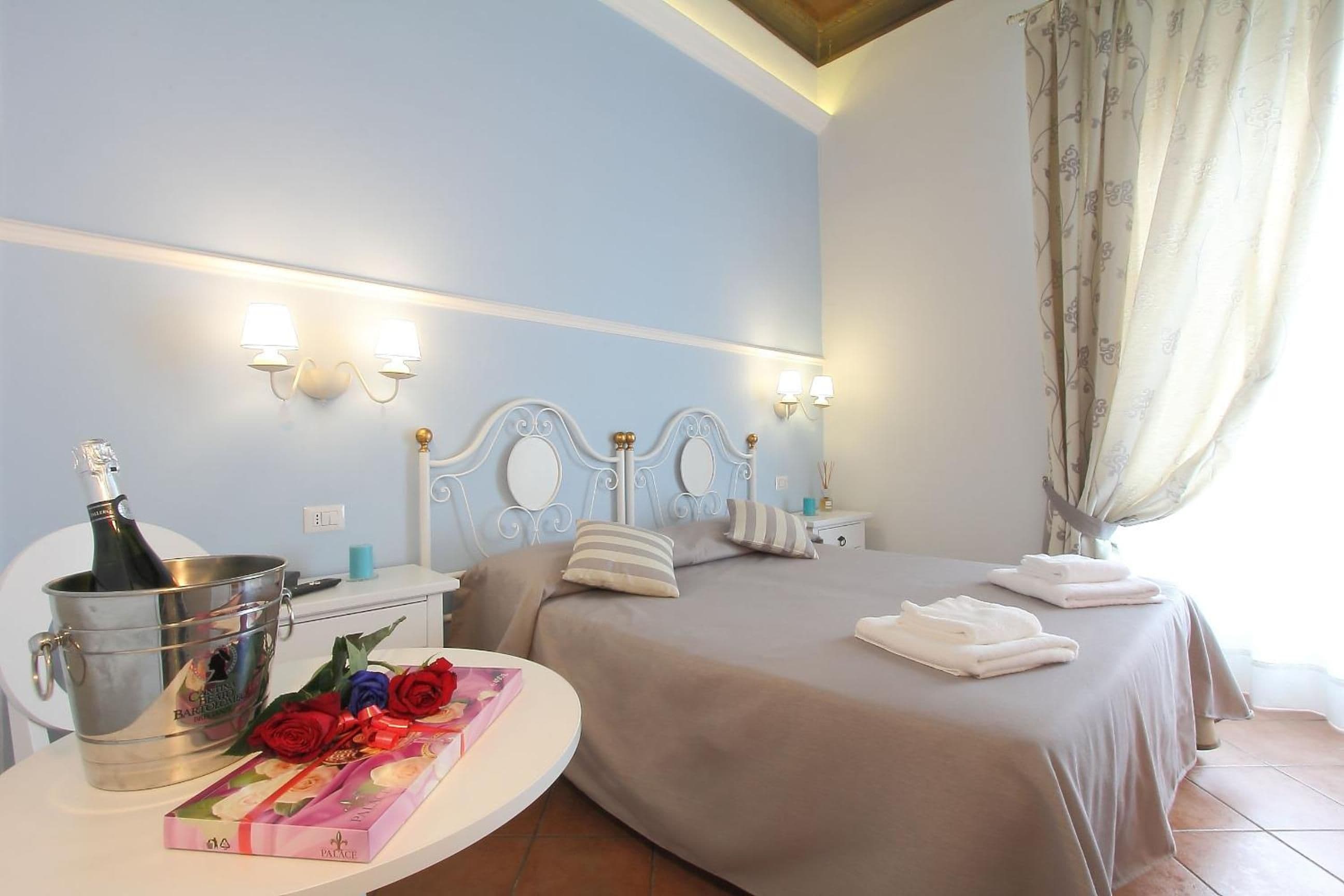 Ein Hotelzimmer mit einem Bett, Nachttischen, einer Flasche Champagner und einem Rosenstrauß.