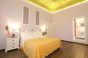 Een slaapkamer met een bed, nachtkastjes, een spiegel en een zichtbare badkamer door een geopende deur.