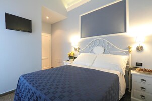 A hotel room with a bed, a flat-screen TV, a nightstand, and a wall-mounted light fixture.