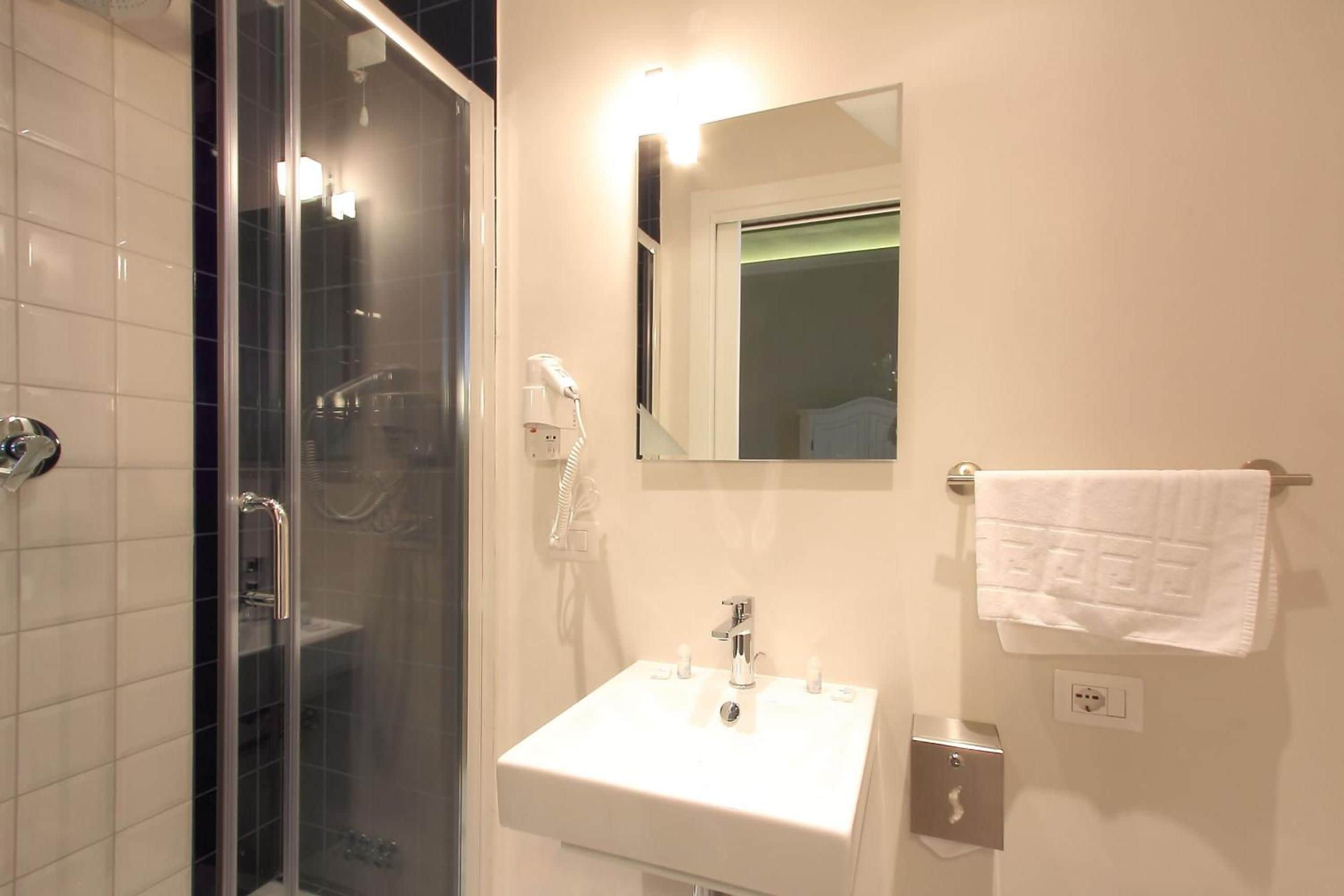 Un baño con ducha de vidrio, lavamanos blanco y toallero.