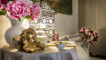 Una mesa con una figurita decorativa de un ángel, un florero con flores rosas, un farolillo y un cuenco de frutas.