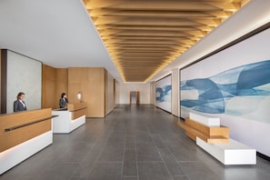 A modern reception area with wooden reception desks, a tiled floor, and a large abstract painting on the wall. - Ramada Plaza by Wyndham Pu Dong South Shanghai (Shanghai)
