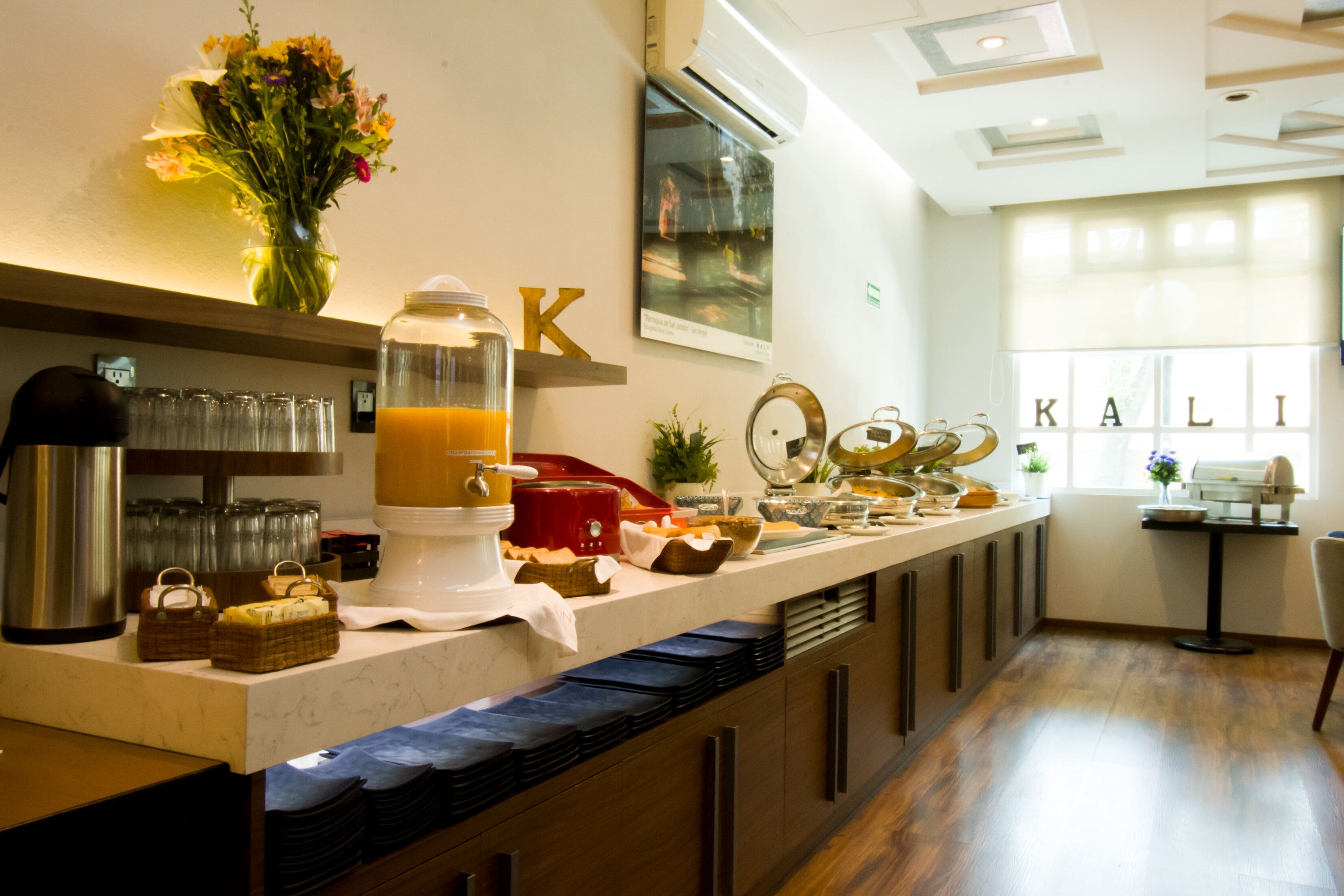 A breakfast bar with a variety of food items, a coffee machine, and a vase of flowers.
