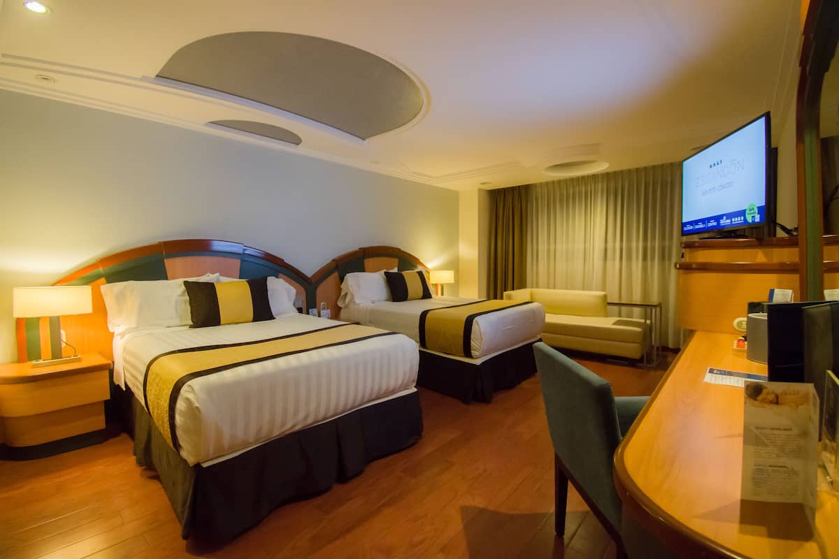 Ein Hotelzimmer mit zwei Betten, einem Schreibtisch, einem Fernseher und einem Sessel.
