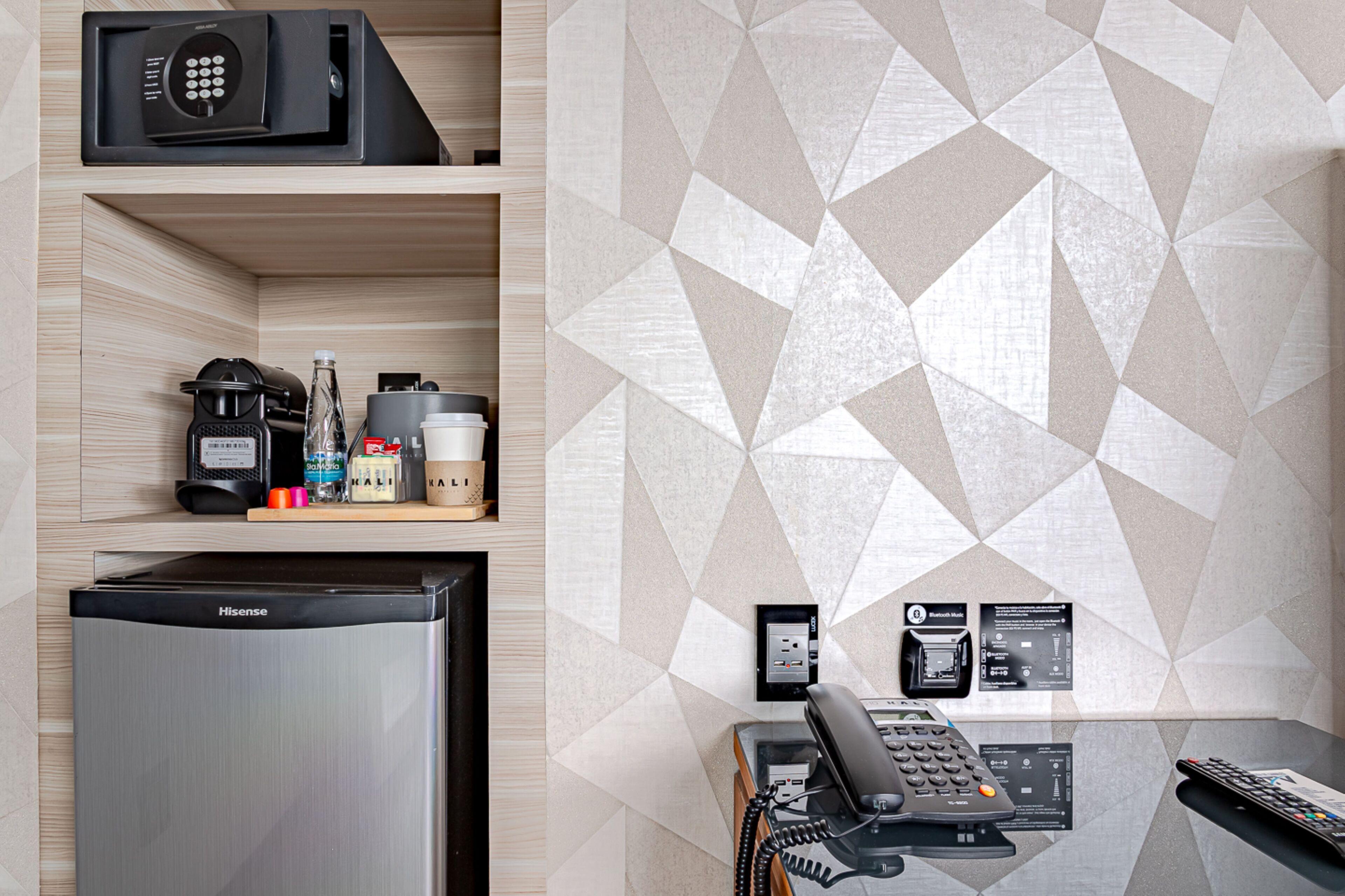 A hotel room with a minibar, a Hisense refrigerator, a coffee maker, and a geometric-patterned wall.