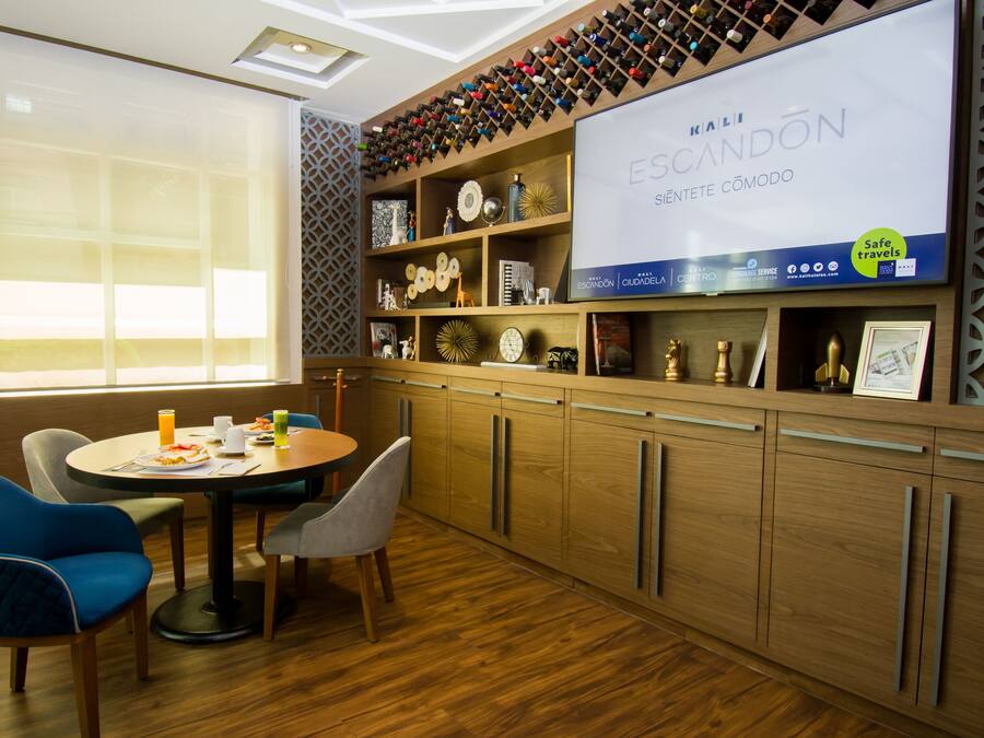 Habitación de hotel moderna con piso de madera, un área de comedor con una mesa redonda y sillas, y una repisa de pared con diversos objetos decorativos.