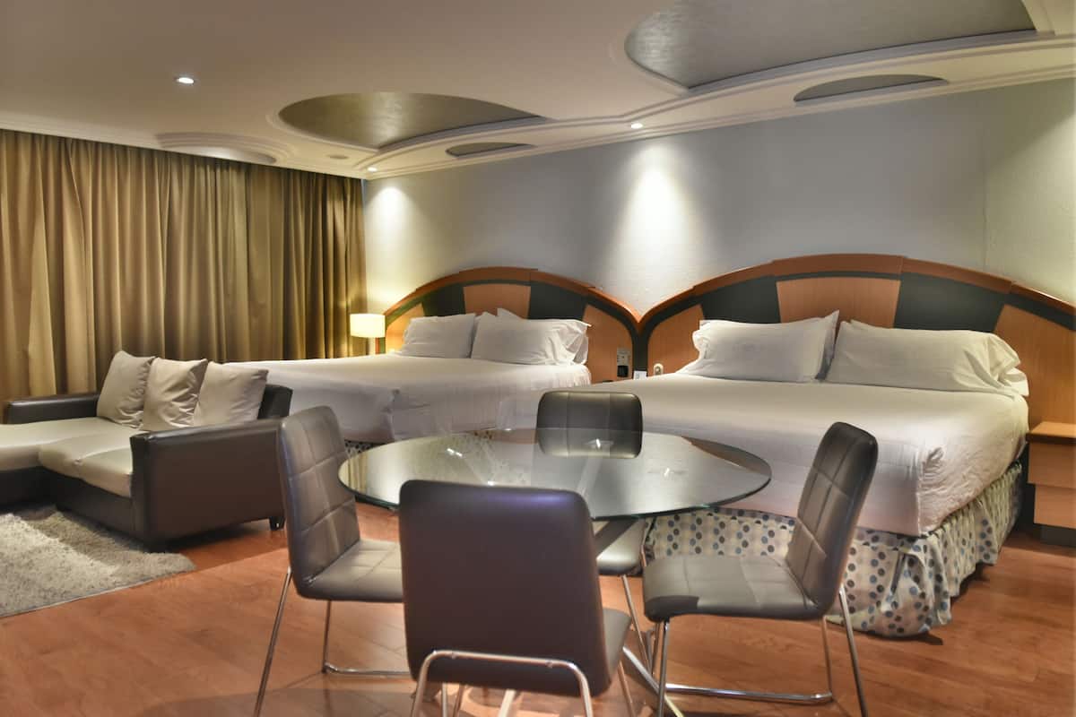 Ein Hotelzimmer mit zwei Betten, einem runden Glastisch und einer Couch.