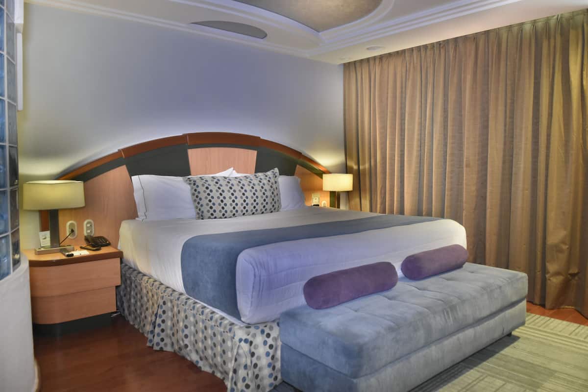 Ein Hotelzimmer mit einem großen Bett, einem Nachttisch mit Lampe und einem Vorhang.