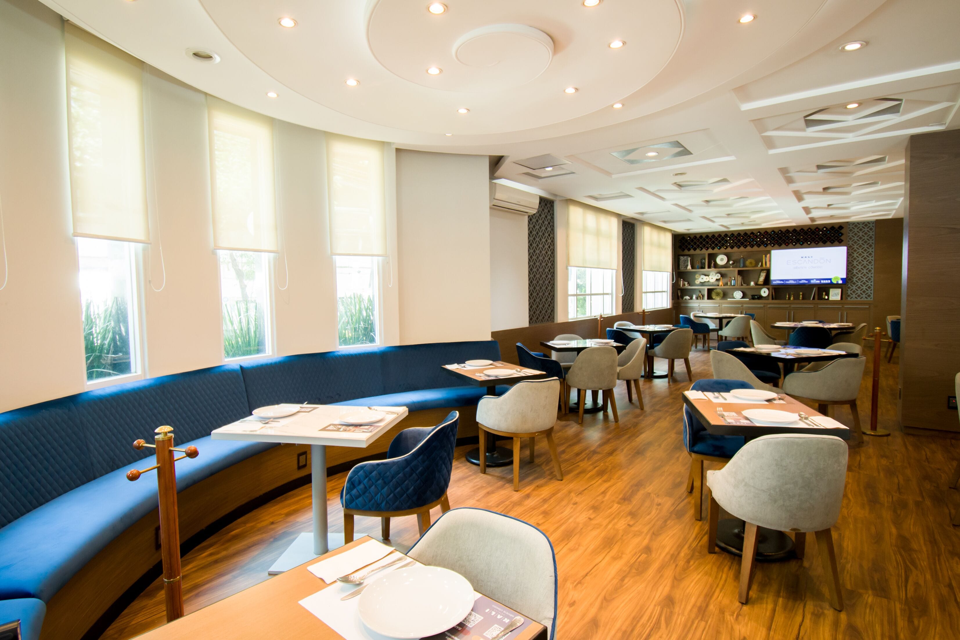 A modern restaurant with a curved blue bench seating area, wooden tables, and a variety of chairs.