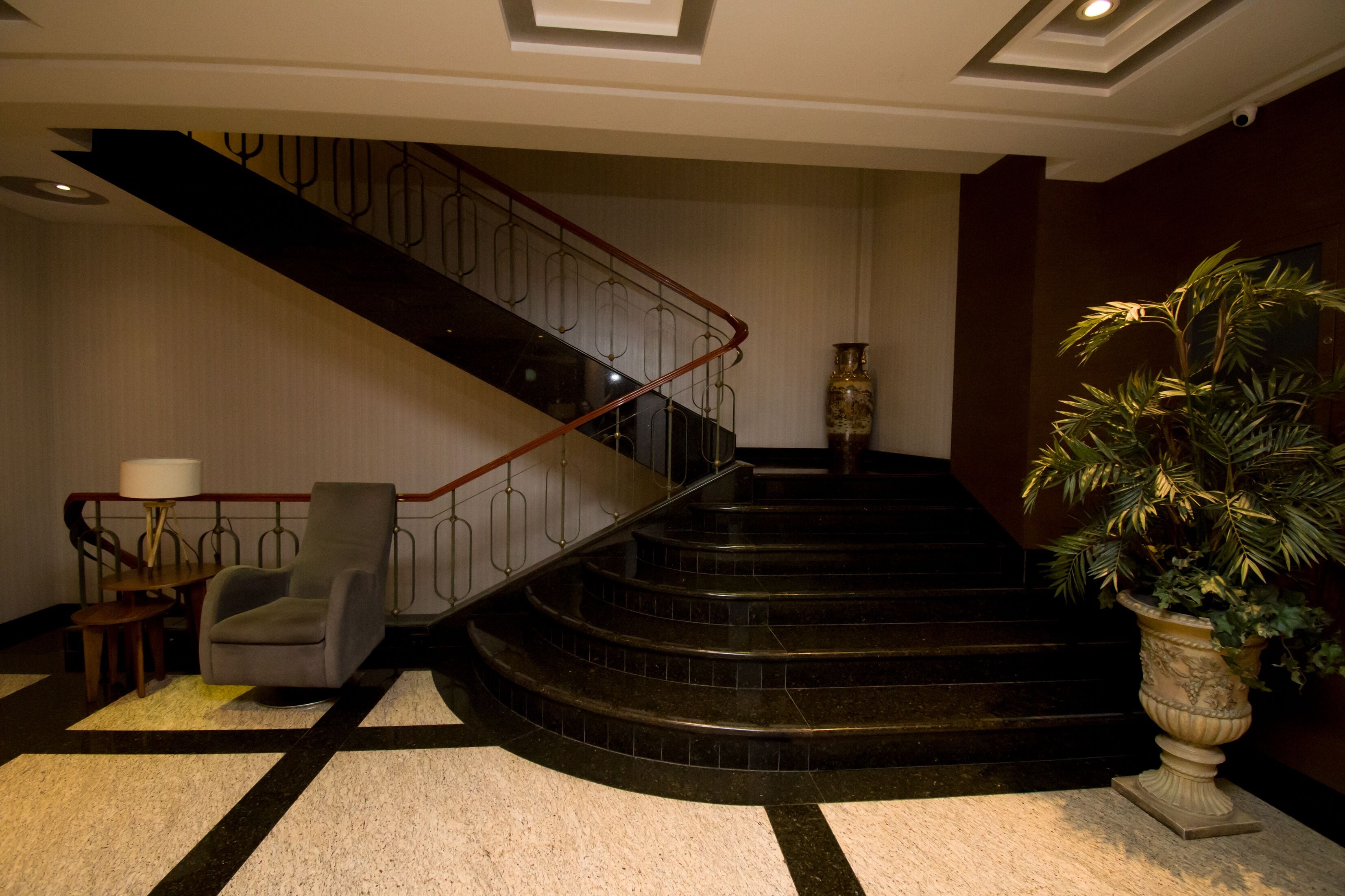 Eine Hotellobby mit einer geschwungenen Treppe, einer Sitzecke mit Sessel und Tisch sowie einer großen Topfpflanze.