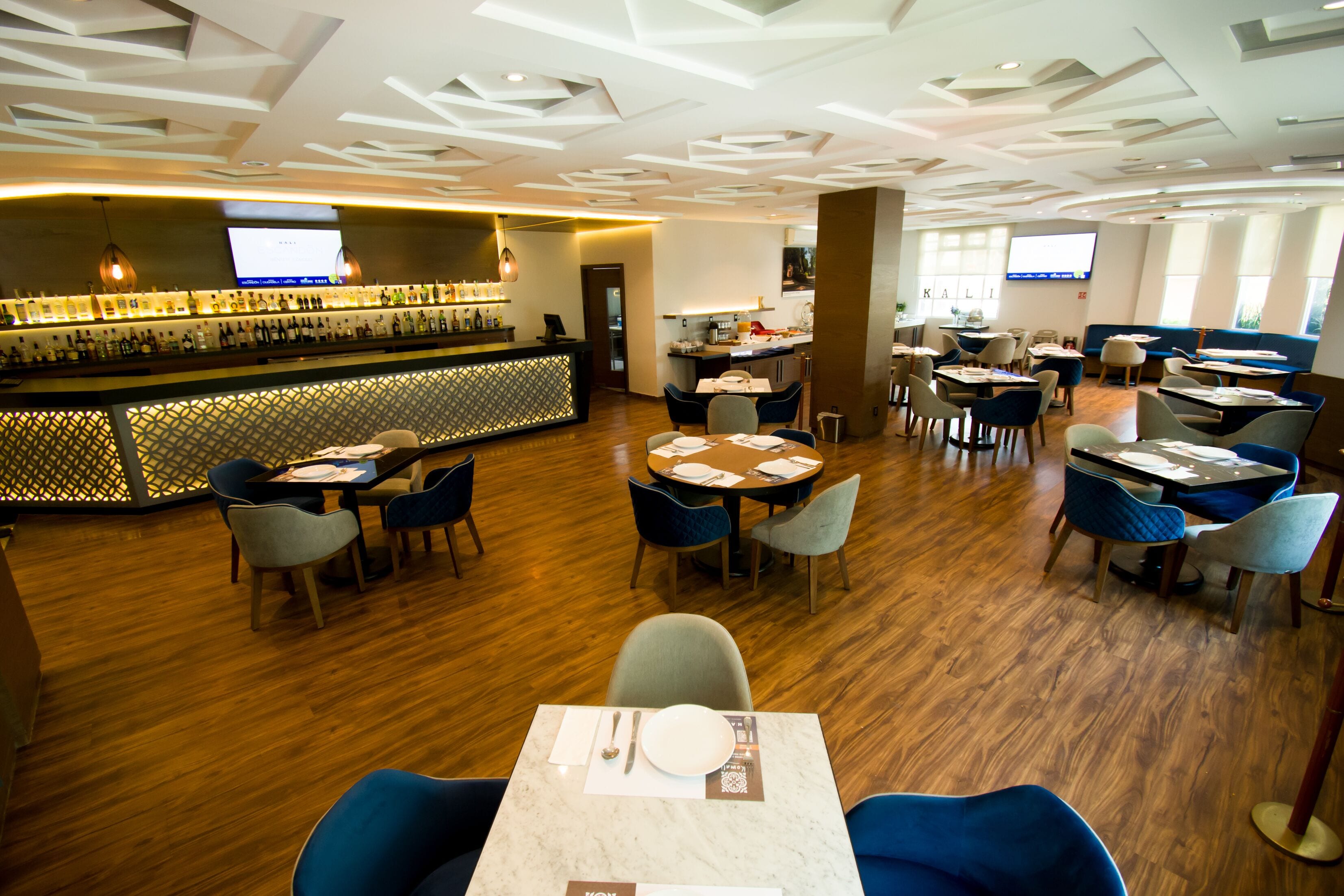 A modern restaurant with a bar area, wooden flooring, and a variety of seating options including tables and chairs.