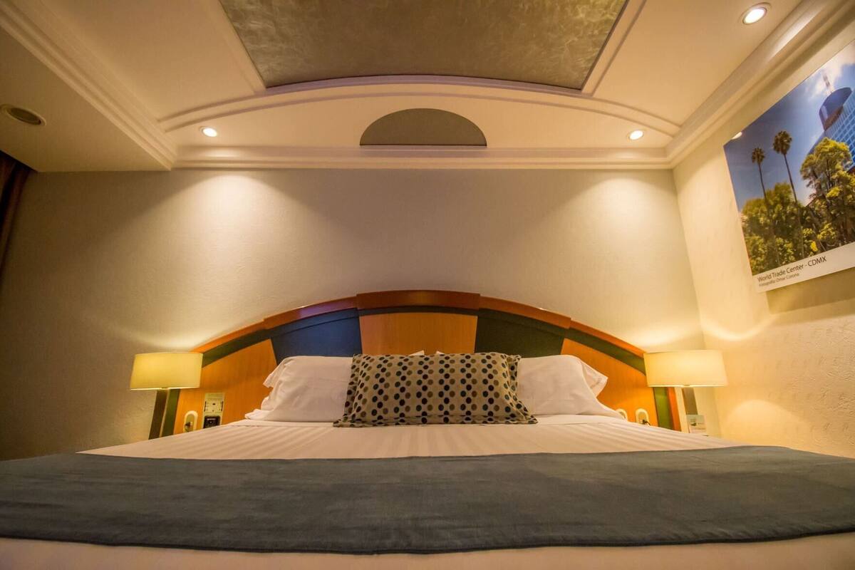 Ein Hotelzimmer mit einem Bett, zwei Nachttischlampen, einer Kopfteil mit geschwungener Form und einer Decke mit Einbautenleuchten.