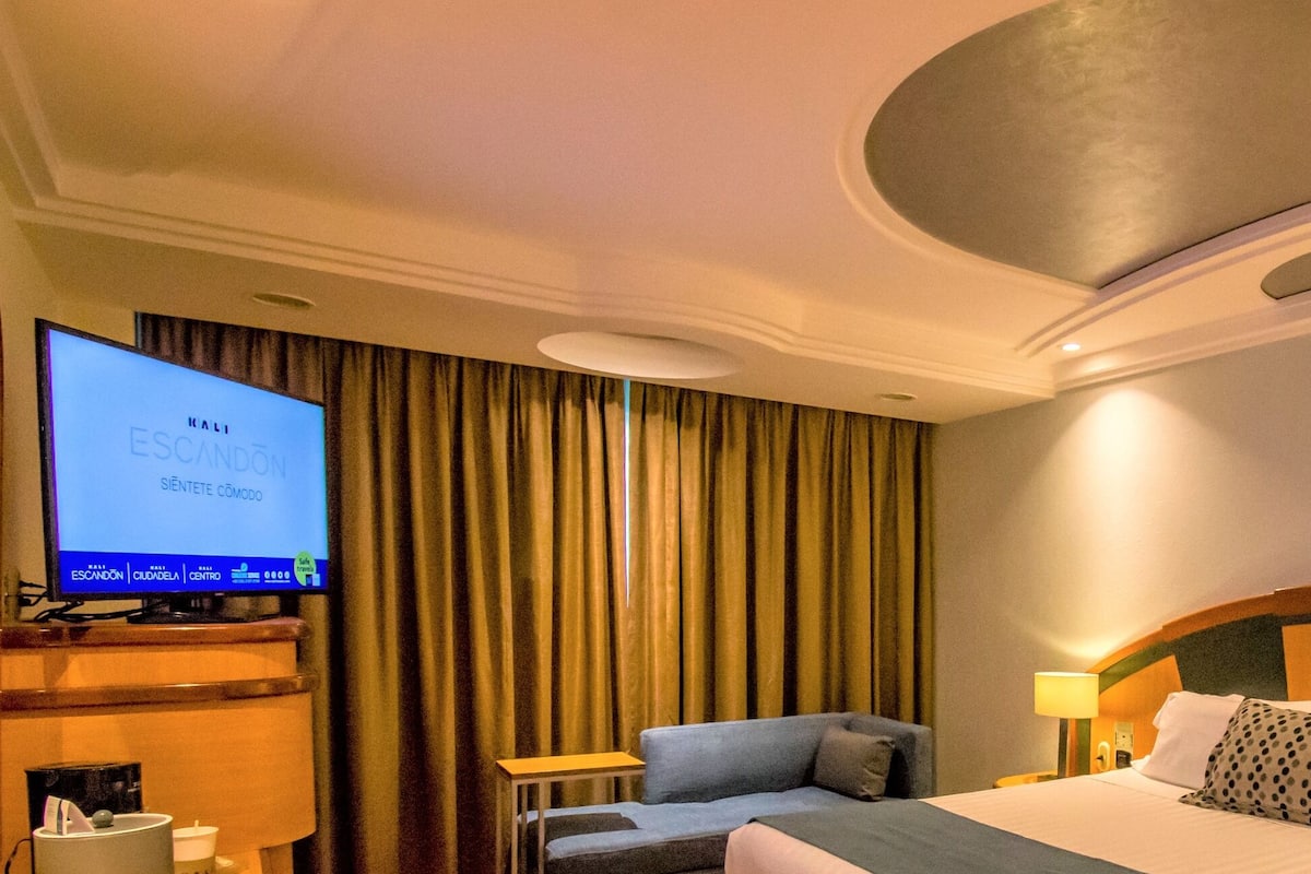 Ein Hotelzimmer mit einem Bett, einem Fernseher auf einem Standfuß, einer Couch und einem Vorhang.