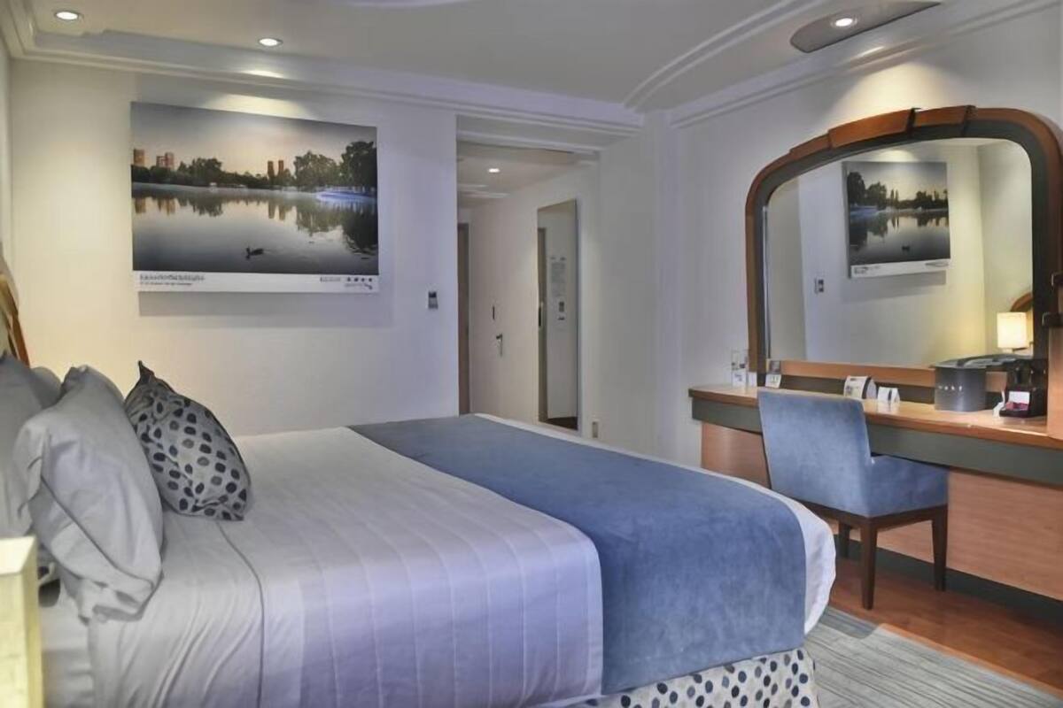 Ein Hotelzimmer mit einem großen Bett, einem Schreibtisch, einem Sessel, einem Spiegel und zwei gerahmten Bildern an der Wand.
