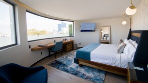 A modern hotel room with a curved wall, a large window, a desk, a bed, and a TV mounted on the wall. - KALI Escandon Mexico City (Mexico City)