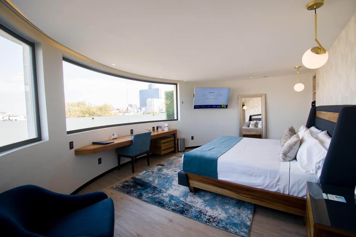 Ein modernes Hotelzimmer mit bogenförmiger Wand, großem Fenster, Schreibtisch, Bett und Wand-Fernseher.