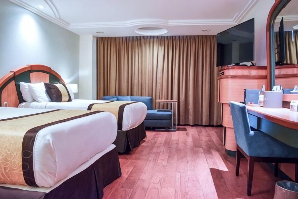 A hotel room with two beds, a desk, a chair, and a television.