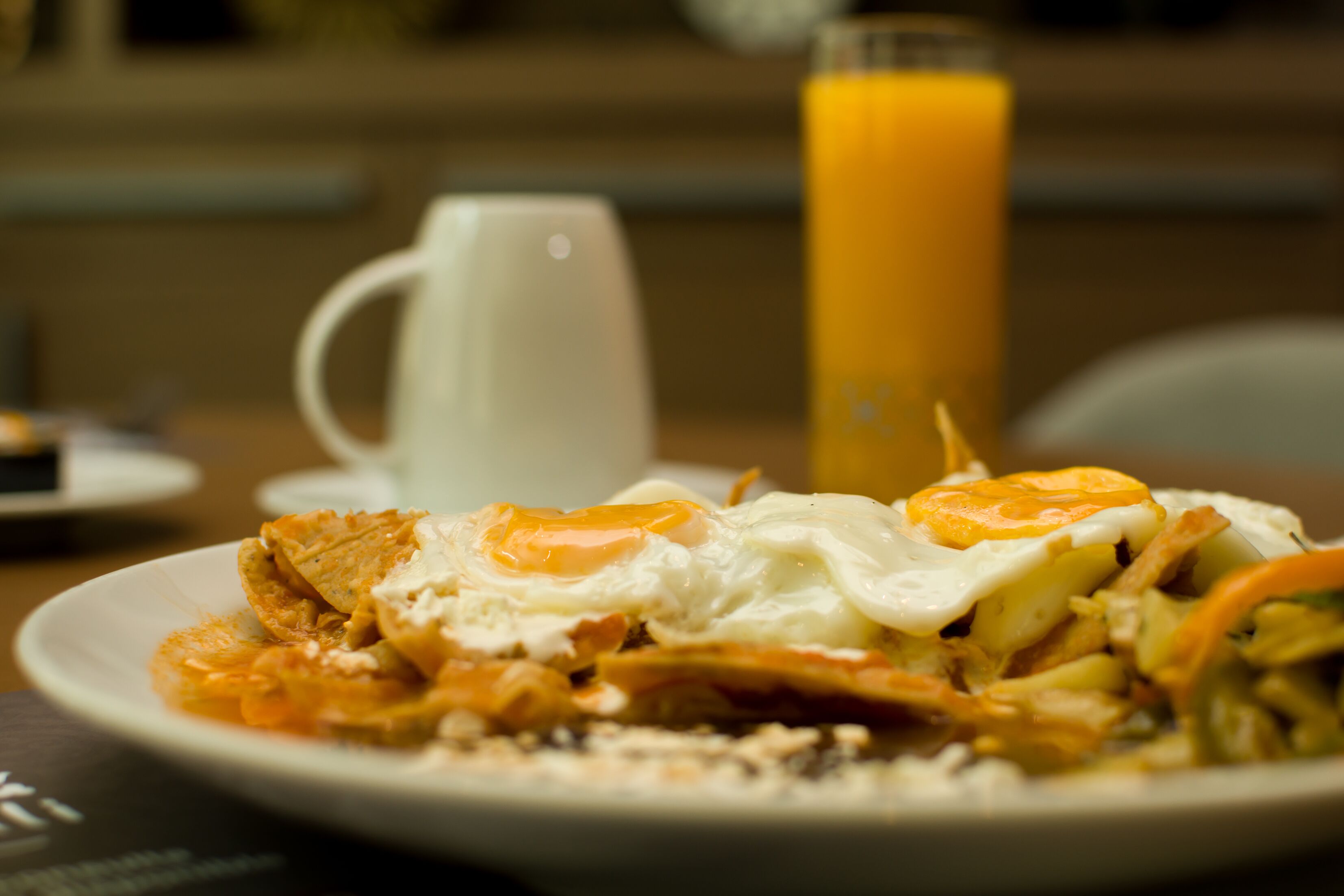 Une assiette remplie de nourriture, avec des œufs et des légumes, un verre de jus d’orange et une tasse blanche posée sur une table.