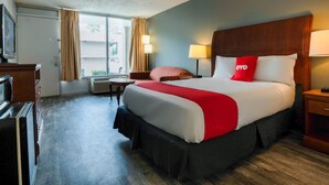 A hotel room with a large bed, a desk, a chair, a TV, and a window with curtains.
