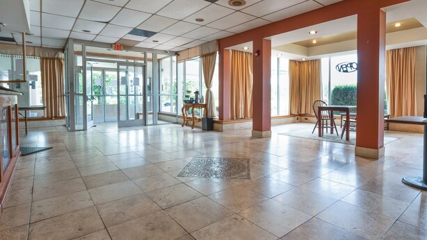 A spacious lobby with a tiled floor, glass doors leading outside, and a seating area with tables and chairs.