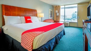 A hotel room with a large bed, a television, a desk, and a window with curtains.