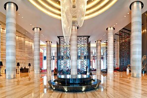 A modern lobby with high ceilings, large cylindrical columns, a central reflective water feature, and a reception desk. - Le Meridien Chongqing, Nan'an (Chongqing)