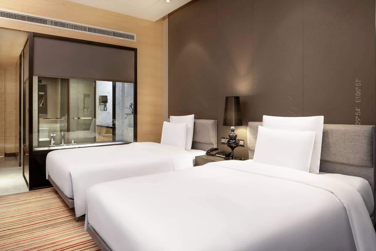 Ein Hotelzimmer mit zwei Betten, einem großen Spiegel, einem Nachttisch mit Lampe und Blick ins Badezimmer.
