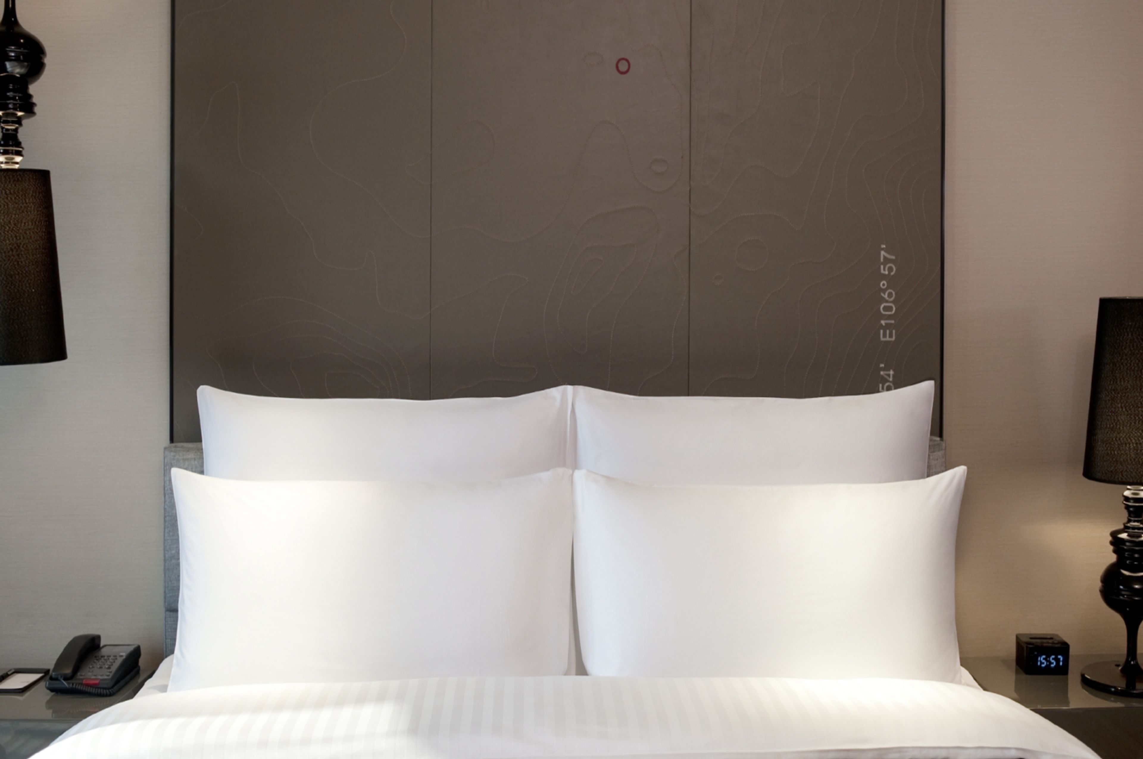Een hotelkamer met een groot bed, een nachtkastje met een lamp, een telefoon en een digitale klok.