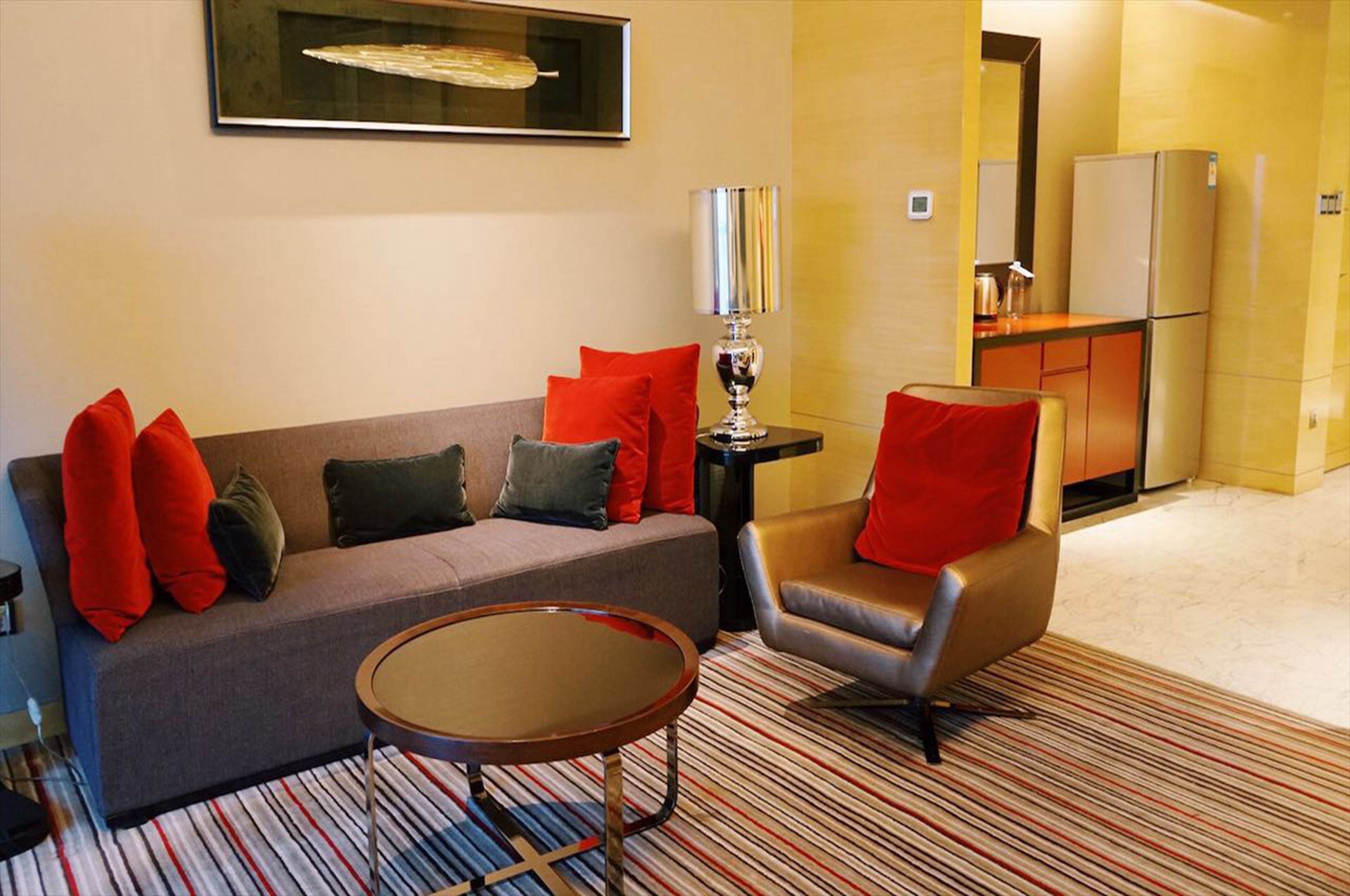 Una sala moderna con sofá, sillón y mesa de centro, una zona de cocina con refrigerador y un tapete a rayas.