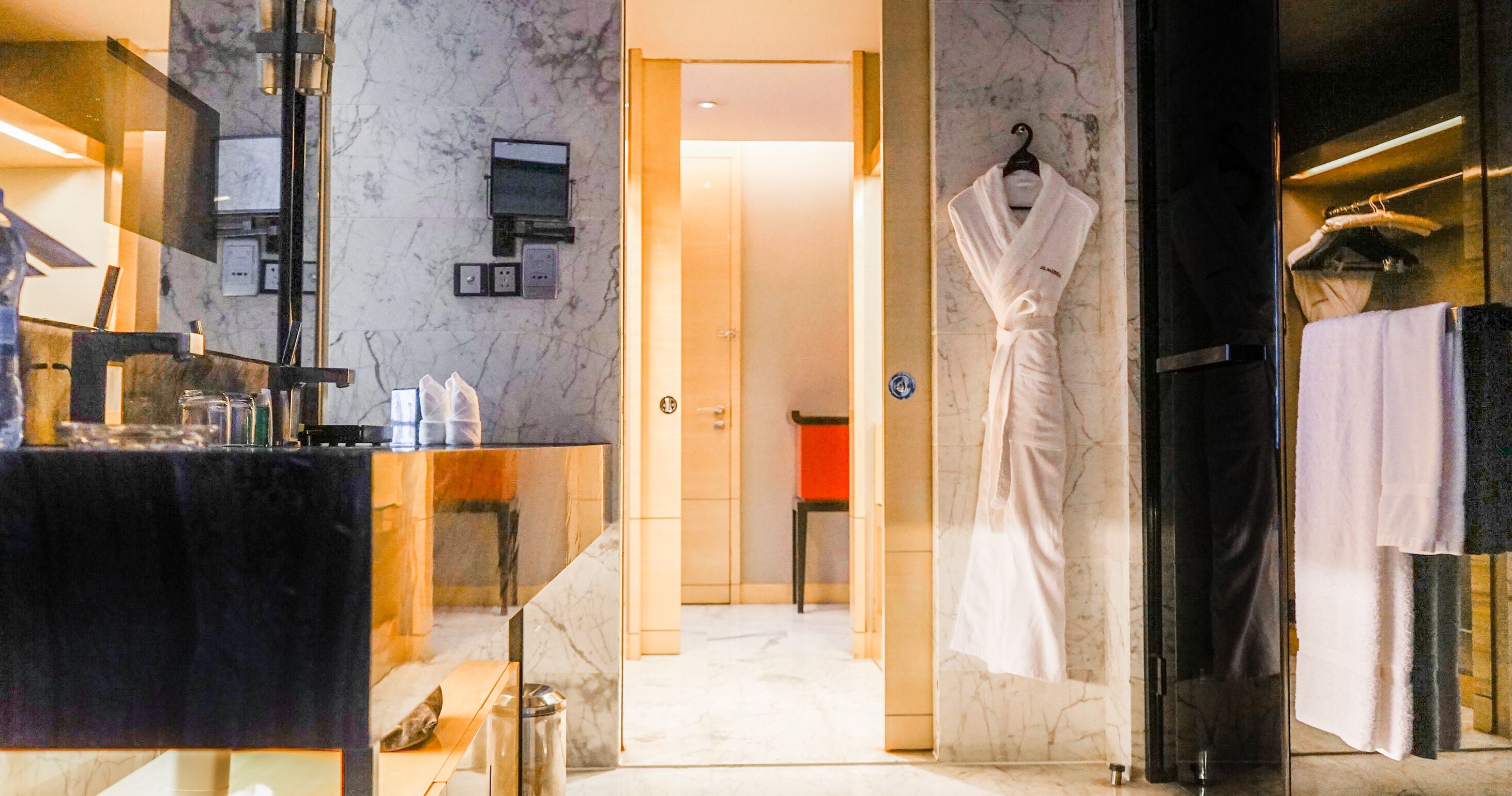 Un baño de hotel con pared de mármol, un lavabo y una bata colgada en la pared.