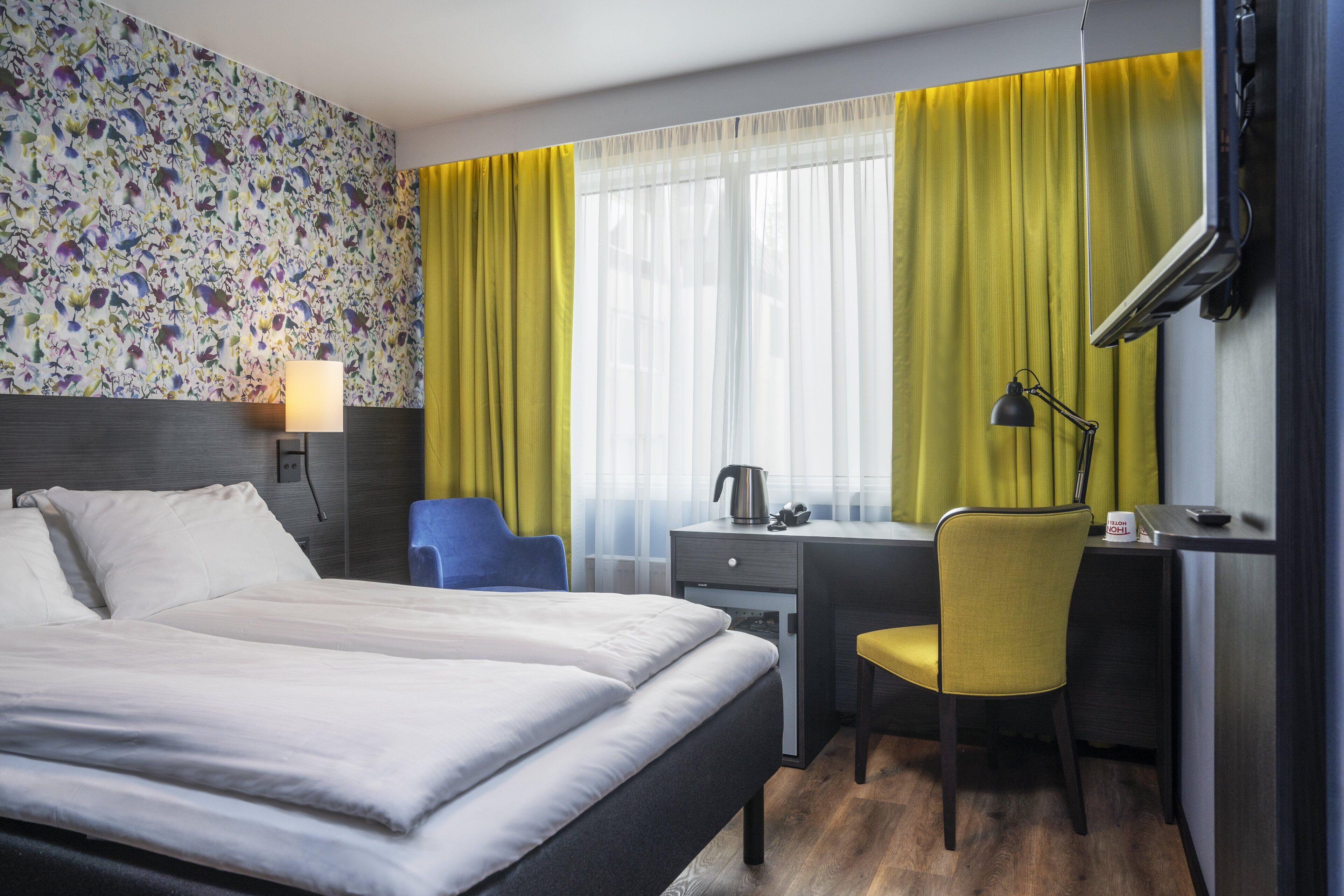Hotelkamer met een bed, bureau, stoel, lamp en raam met gordijnen.