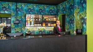 A bar area with a bartender, shelves stocked with beverages, and a decorative wall with a tropical pattern. - Thon Hotel Tromsø (Tromsø)