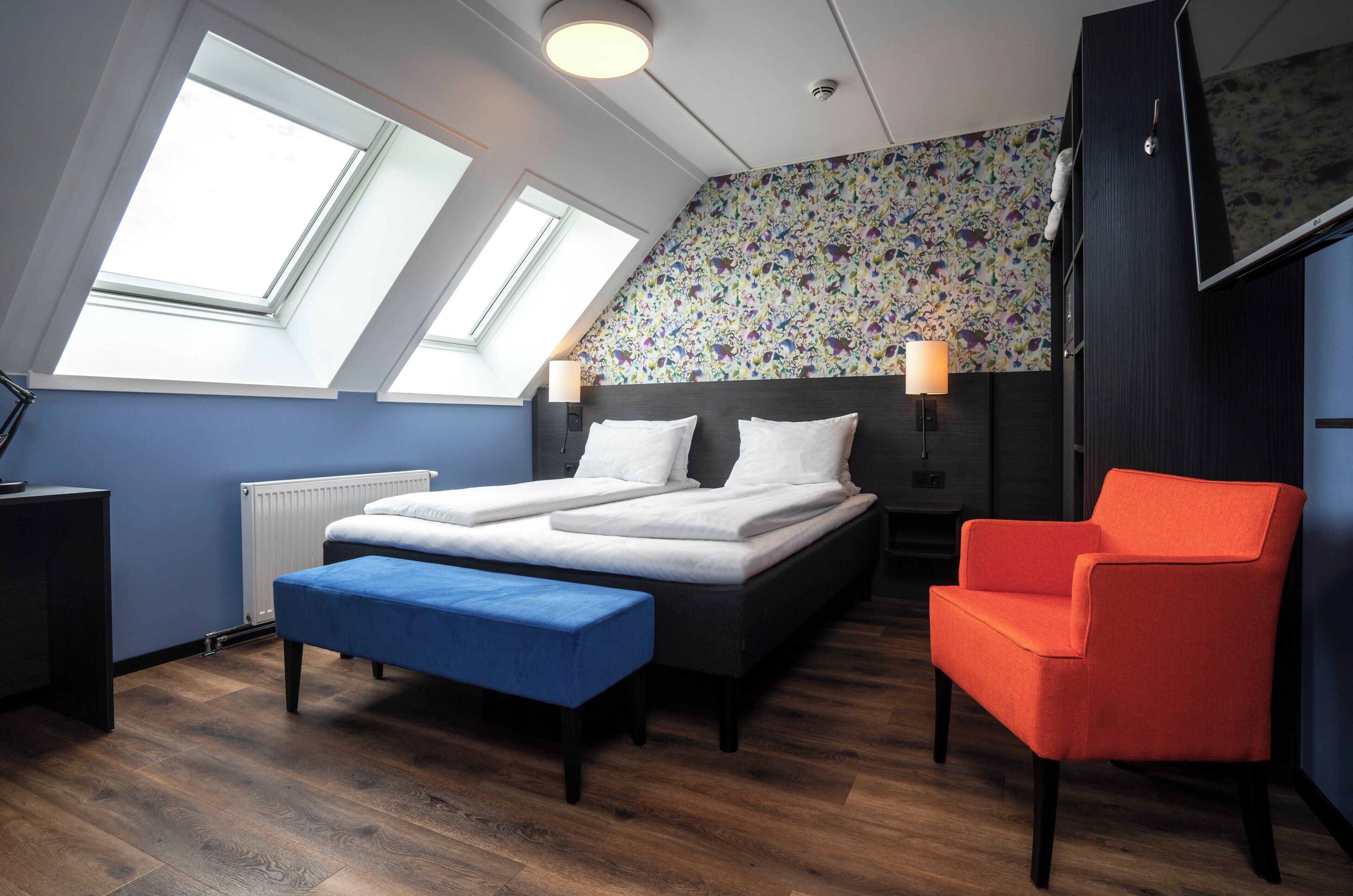 Een slaapkamer met een bed, een bankje, een stoel en een radiator.