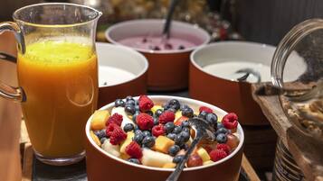 Een ontbijtsetting met een glazen kan sinaasappelsap, bakjes yoghurt met fruit, en een pot granola.