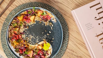 A plate of food with various fruits and seeds on a woven placemat, accompanied by a book titled "Nourish Your Skin From The Inside Out".
