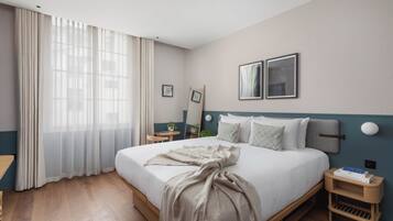 A neatly made bed with a blanket, a bedside table with a book, and a wall-mounted picture frame.