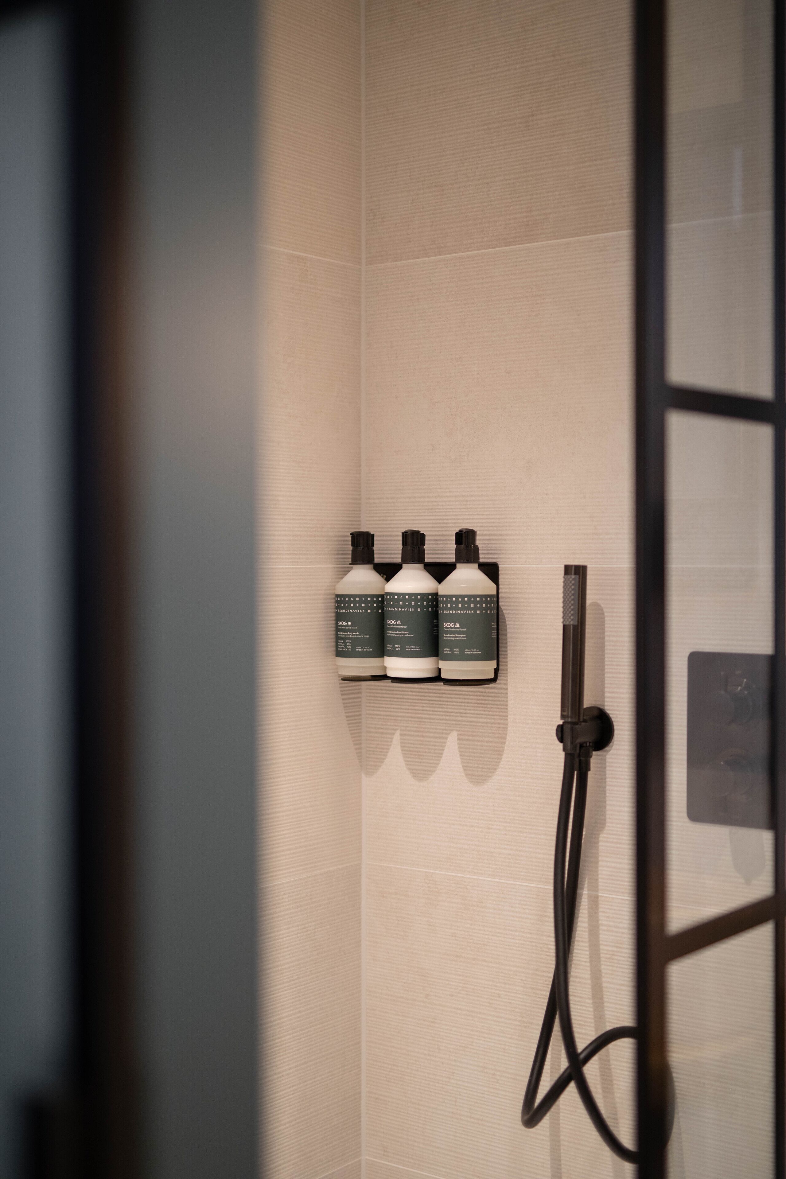 A shower area with three bottles of shampoo and a handheld showerhead.