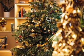 A Christmas tree with ornaments and lights in a room with shelves and a potted plant. - Inhabit Queen's Gardens, a Member of Design Hotels (London)