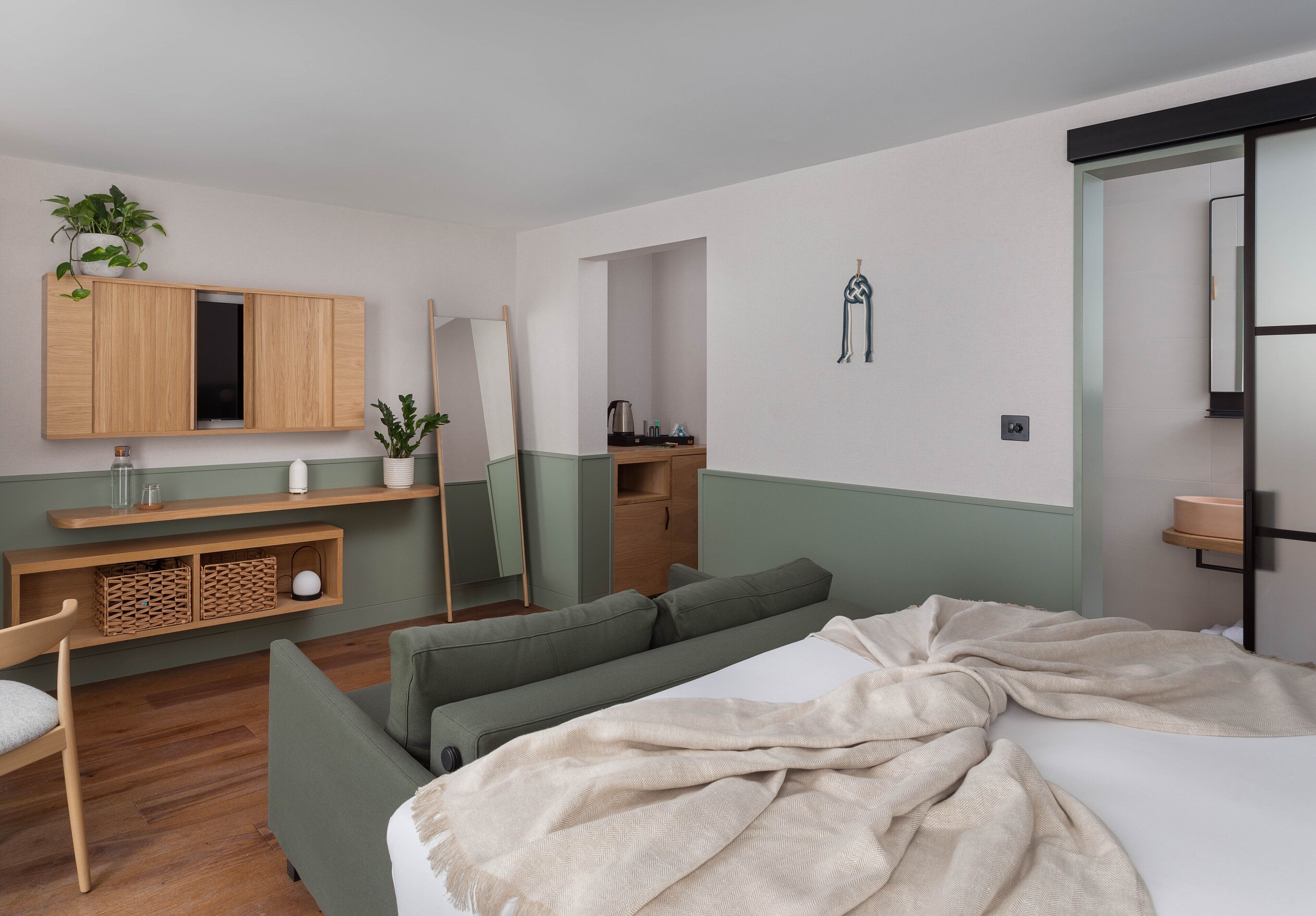 Un dormitorio moderno con cama, sofá, mueble de madera con espejo y una pequeña zona de kitchenette.