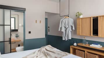 A hotel room with a bed, a wooden vanity, a hanging robe, a mirror, and a bathroom visible through a sliding door.