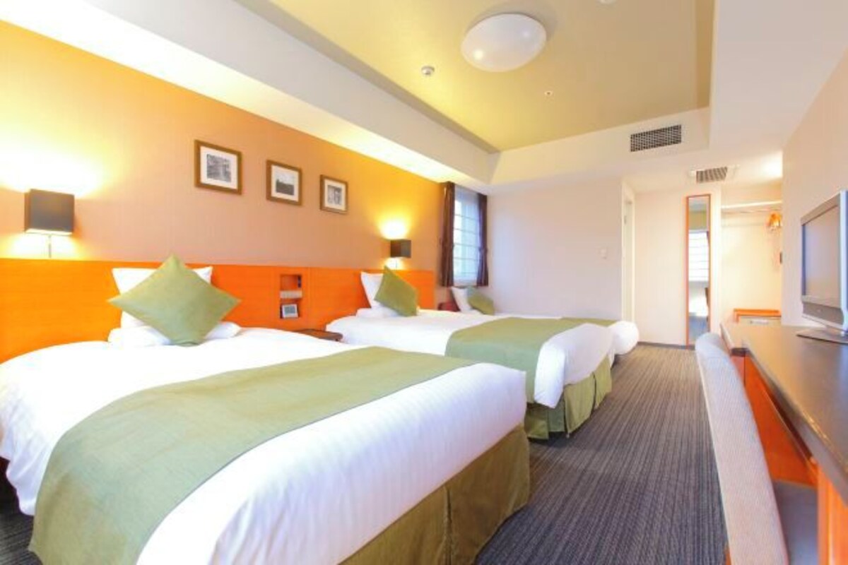 Habitación de hotel con dos camas, un escritorio y una televisión.