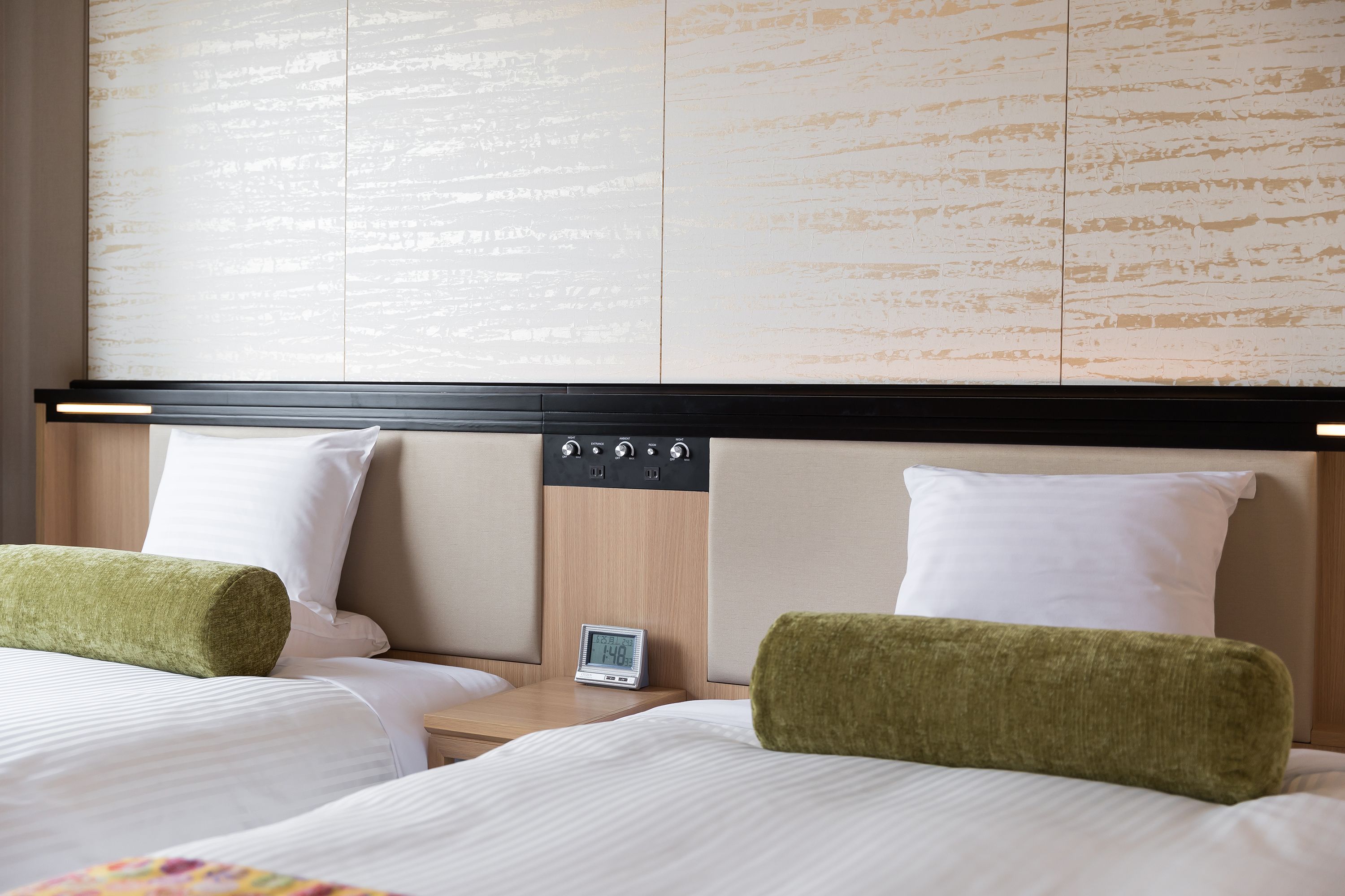 Una habitación de hotel con dos camas, un cabecero de madera, un reloj digital y una mesita de noche.