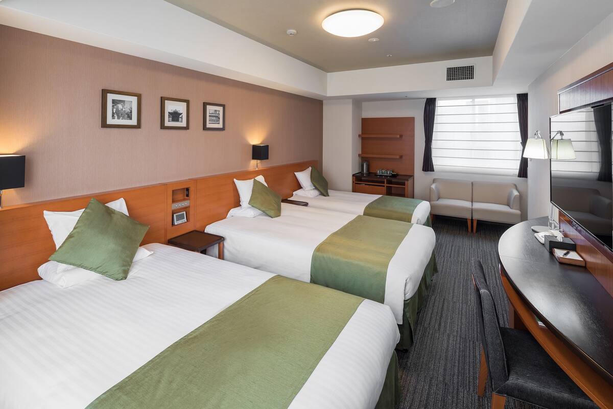A hotel room with two beds, a desk, a TV, and a seating area.