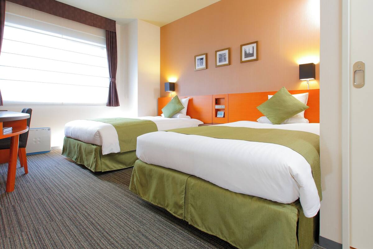 A hotel room with two beds, a desk, and a window with curtains.