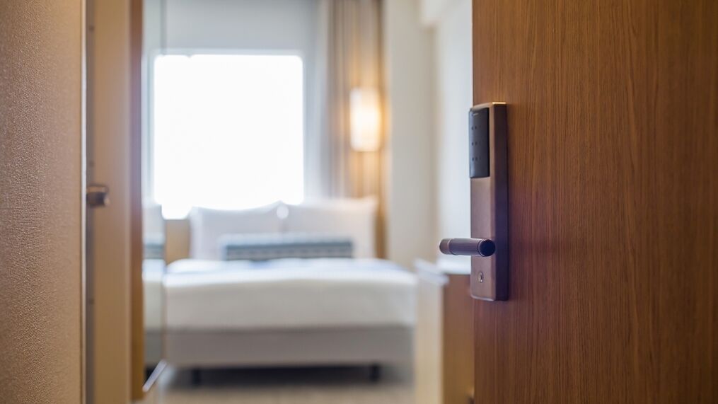 A hotel room with a bed, a bedside table, and a door with a lock.