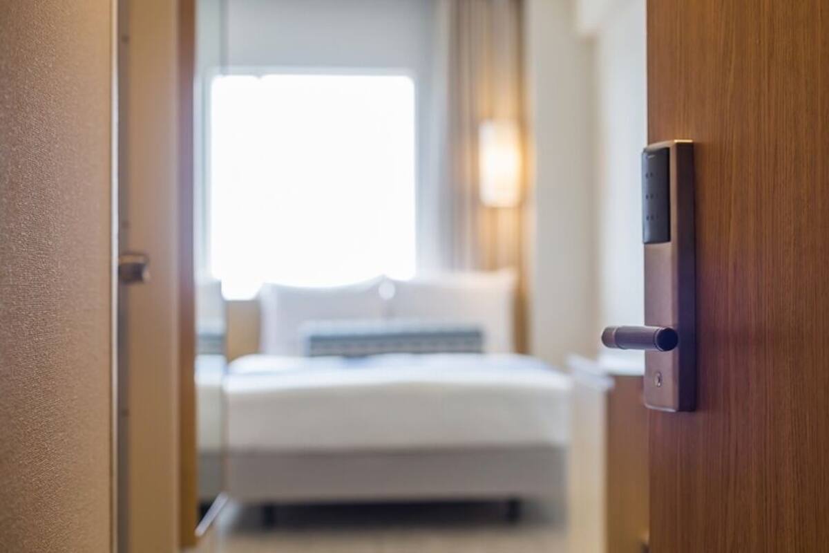 A hotel room with a bed, a bedside table, and a door with a lock.