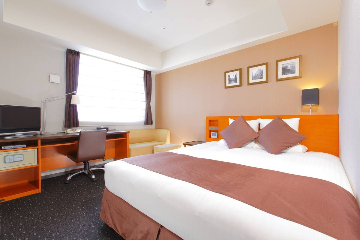 A hotel room with a large bed, a desk with a computer, a chair, and a television.