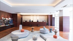 A modern reception area with a wooden reception desk, several seating options, and a display of products on the left. - Hotel MyStays Kyoto - Shijo (Kyoto)