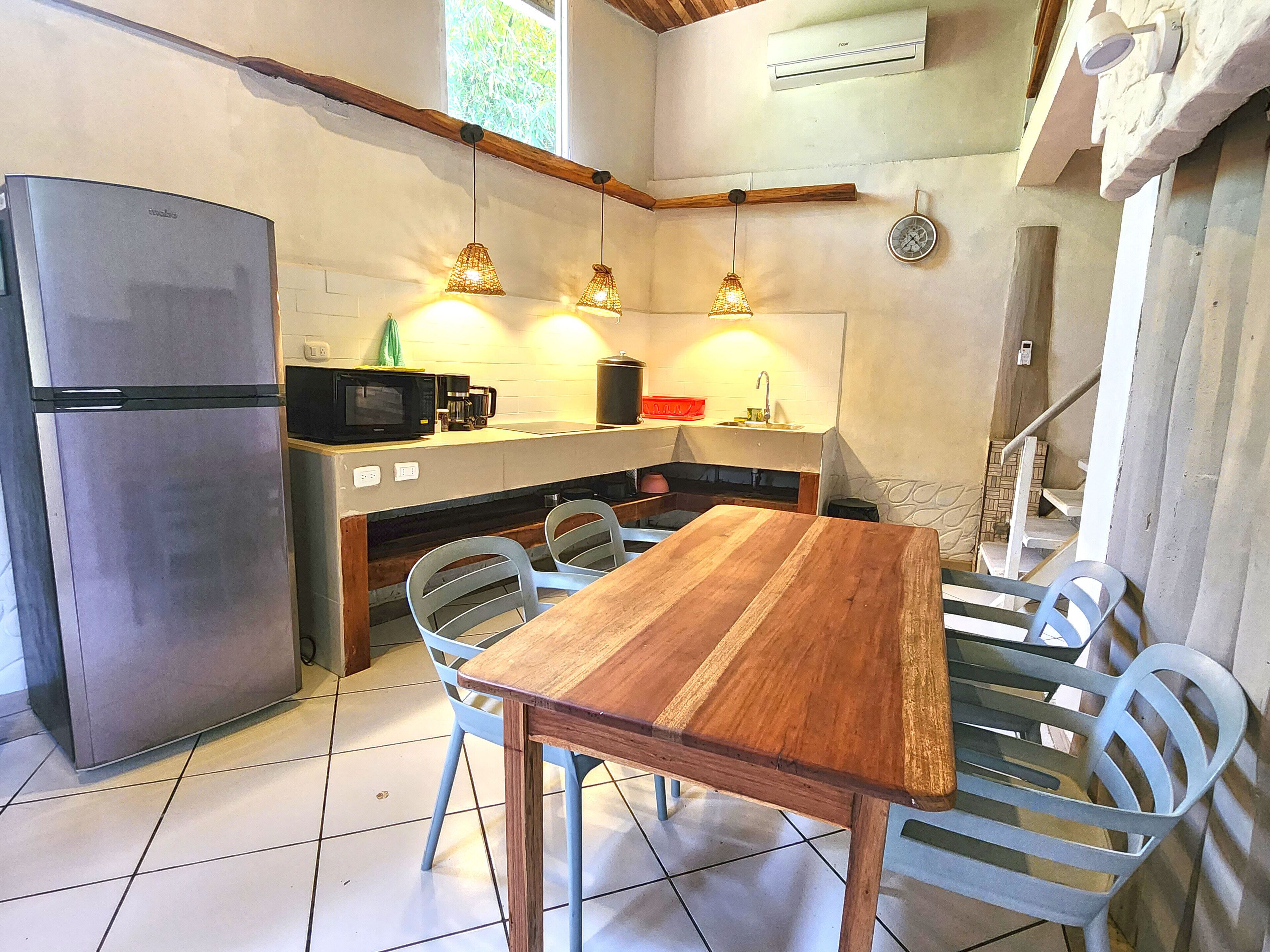 A compact kitchen with a refrigerator, microwave, sink, and wooden dining table with chairs.